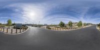 a street with a curve and the sun over it in a sky with clouds and blue sky