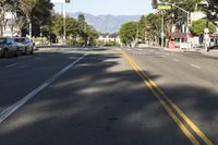 an empty street with cars parked along the side of it and a mountain in the background