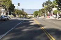 an empty street with cars parked along the side of it and a mountain in the background