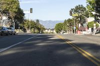 an empty street with cars parked along the side of it and a mountain in the background