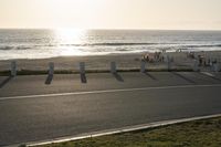 an empty road near a beach and waves as well as cars on the sand and houses on the beach