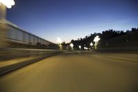 street lights from vehicle on overpass overlooking trees at dusk at dusk in background, blurry image