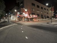 an empty street near the building with its neon sign in front of it at night