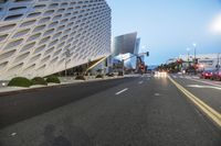 an empty street with a white building on the other side of it and cars in front of it