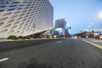 an empty street with a white building on the other side of it and cars in front of it