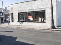 a man is walking past a restaurant on the side of the street behind a parked car