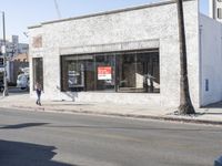 a man is walking past a restaurant on the side of the street behind a parked car