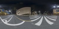 an intersection with the city hall in the background at night, seen in fisheye mode