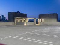 a parking garage with white lines in the parking lot at dusk, overlooking a city