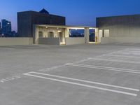 a parking garage with white lines in the parking lot at dusk, overlooking a city