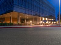 a city street with buildings at night with lights on and an empty sidewalk near the curb