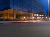 a city street with buildings at night with lights on and an empty sidewalk near the curb