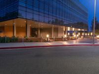 a city street with buildings at night with lights on and an empty sidewalk near the curb