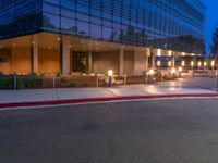 a city street with buildings at night with lights on and an empty sidewalk near the curb