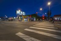 traffic lights illuminate a street at night time as an advertisement is seen on the wall