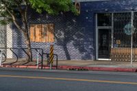 an empty street with three wooden chairs in front of a storefront window with a few people nearby