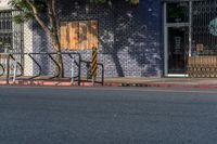 an empty street with three wooden chairs in front of a storefront window with a few people nearby