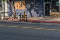 an empty street with three wooden chairs in front of a storefront window with a few people nearby