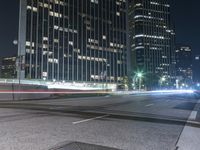 an empty city street at night with light streaks on the side and skyscrapers on one side