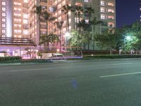 a tall white building with cars parked in front of it at night time on the streets