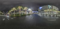 an empty street at night under some lights and palm trees around it with buildings on both sides