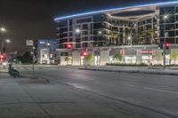 an empty street at night with some cars parked on the side of it and illuminated lights on