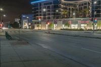 an empty street at night with some cars parked on the side of it and illuminated lights on