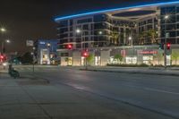 an empty street at night with some cars parked on the side of it and illuminated lights on