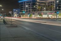 an empty street at night with some cars parked on the side of it and illuminated lights on