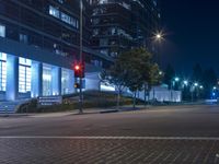 the red traffic light is on at night in an urban area by some large buildings