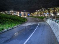 an empty freeway on a very dark night with bright lights on the buildings, bushes and plants near it