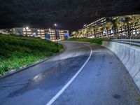 an empty freeway on a very dark night with bright lights on the buildings, bushes and plants near it