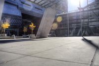 a man skating on cement in an empty area in front of a large building, with trees and other plants