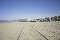 people walk on sand at a beach, near the ocean in the distance is a sky with few cloudless, and blue skies