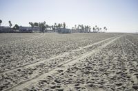 people walk on sand at a beach, near the ocean in the distance is a sky with few cloudless, and blue skies