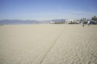 people walk on sand at a beach, near the ocean in the distance is a sky with few cloudless, and blue skies