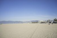 people walk on sand at a beach, near the ocean in the distance is a sky with few cloudless, and blue skies