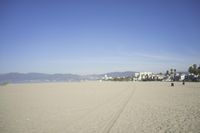 people walk on sand at a beach, near the ocean in the distance is a sky with few cloudless, and blue skies