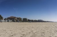 people walk on sand at a beach, near the ocean in the distance is a sky with few cloudless, and blue skies