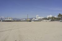 people walk on sand at a beach, near the ocean in the distance is a sky with few cloudless, and blue skies