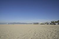 people walk on sand at a beach, near the ocean in the distance is a sky with few cloudless, and blue skies