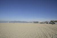 people walk on sand at a beach, near the ocean in the distance is a sky with few cloudless, and blue skies