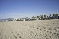 people walk on sand at a beach, near the ocean in the distance is a sky with few cloudless, and blue skies