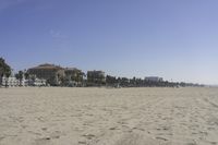 people walk on sand at a beach, near the ocean in the distance is a sky with few cloudless, and blue skies