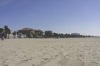 people walk on sand at a beach, near the ocean in the distance is a sky with few cloudless, and blue skies