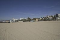 people walk on sand at a beach, near the ocean in the distance is a sky with few cloudless, and blue skies