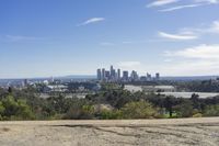 the view of a city skyline from atop of a hill and dirt road below in a city,