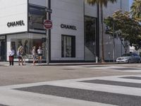 people are walking down a crosswalk in front of the chanel building on the corner