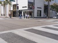 people are walking down a crosswalk in front of the chanel building on the corner