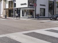 people are walking down a crosswalk in front of the chanel building on the corner